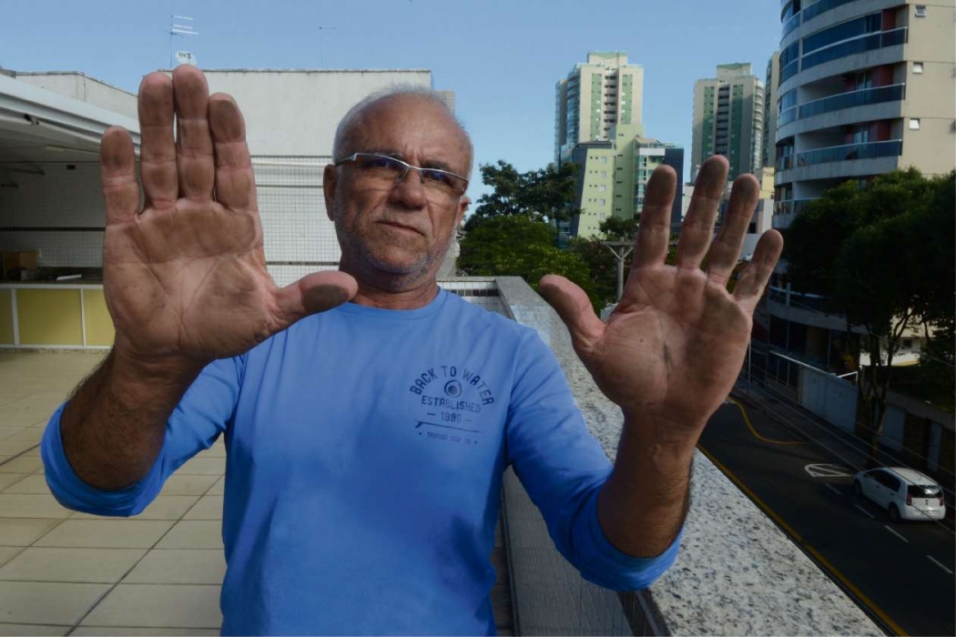 Morador de Jardim Camburi,  Antônio Nascimento mostra as mãos sujas com o pó preto em sua casa
