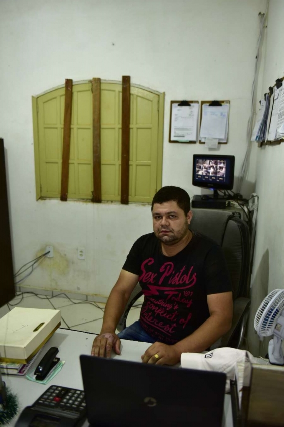 O comerciante Jhonatan de Oliveira, 31, passa o dia trabalhando em uma sala sem circulação de ar. Ripas de madeira foram pregadas na janela para reforçar a segurança do local após três casos de arrombamentos em 2018. "Até as grades eles conseguiram tirar. Agora tem que ficar assim.". Crédito: Marcelo Prest
